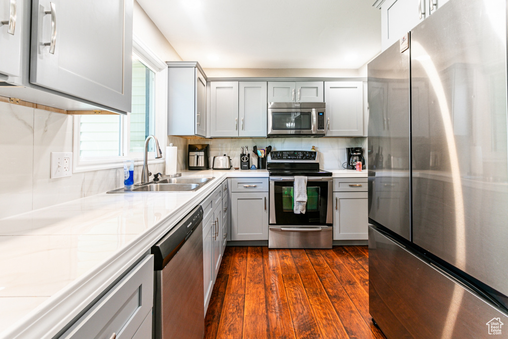 Kitchen with a sink, stainless steel appliances, dark wood finished floors, light countertops, and gray cabinetry