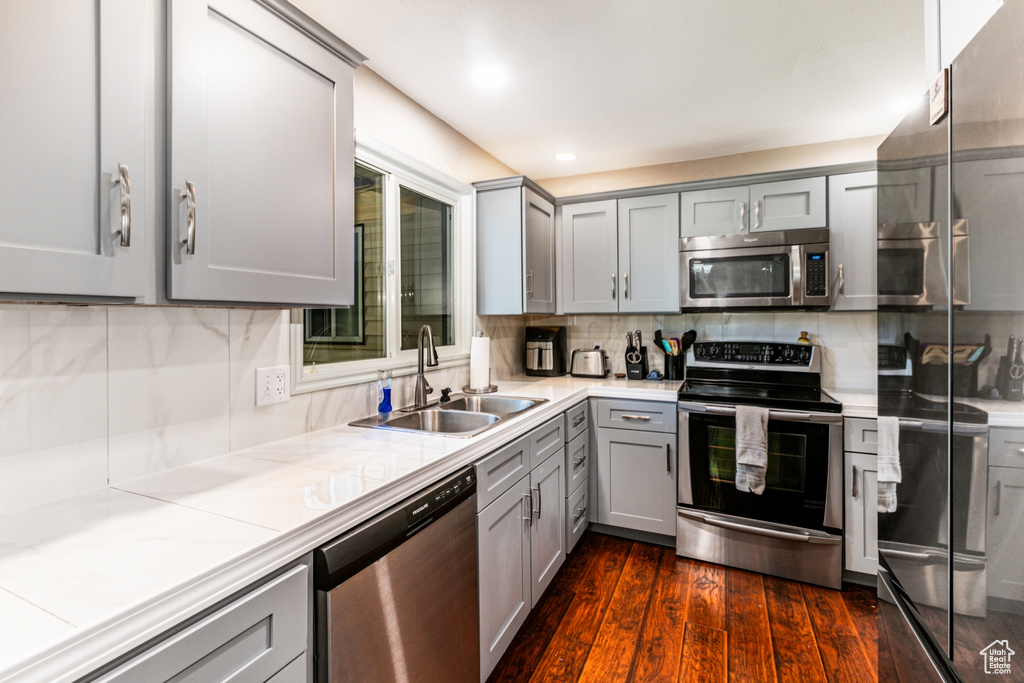 Kitchen with a sink, gray cabinets, dark wood-style flooring, appliances with stainless steel finishes, and decorative backsplash