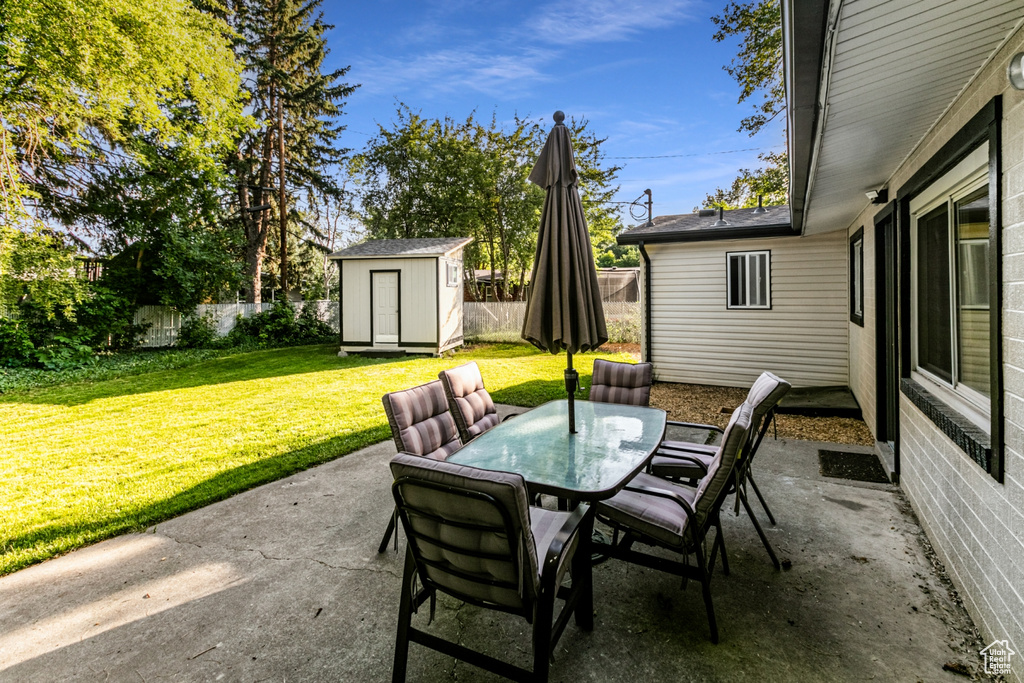 View of patio / terrace featuring an outbuilding, a fenced backyard, outdoor dining space, and a storage unit