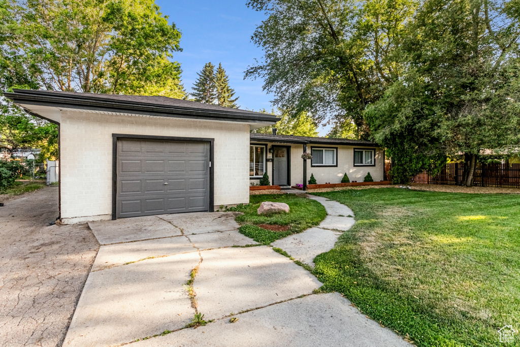 View of front facade featuring an attached garage, fence, a front lawn, brick siding, and driveway