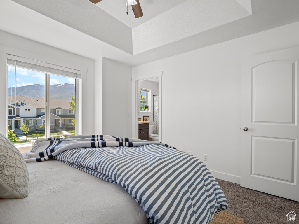 Carpeted bedroom featuring a raised ceiling, baseboards, and a ceiling fan