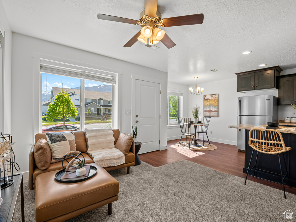 Living area featuring ceiling fan with notable chandelier, a textured ceiling, dark wood finished floors, baseboards, and recessed lighting