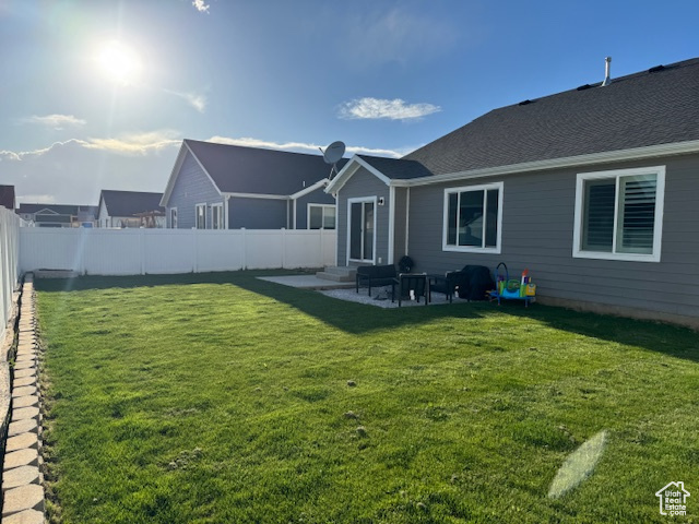 Rear view of house featuring entry steps, a patio, a yard, and a fenced backyard