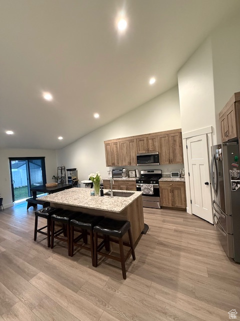 Kitchen with an island with sink, light wood-style flooring, a breakfast bar area, and stainless steel appliances
