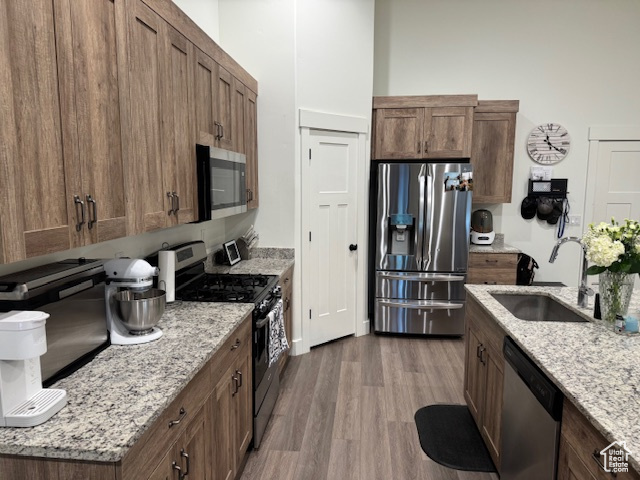 Kitchen with stainless steel appliances, light stone countertops, a sink, and wood finished floors
