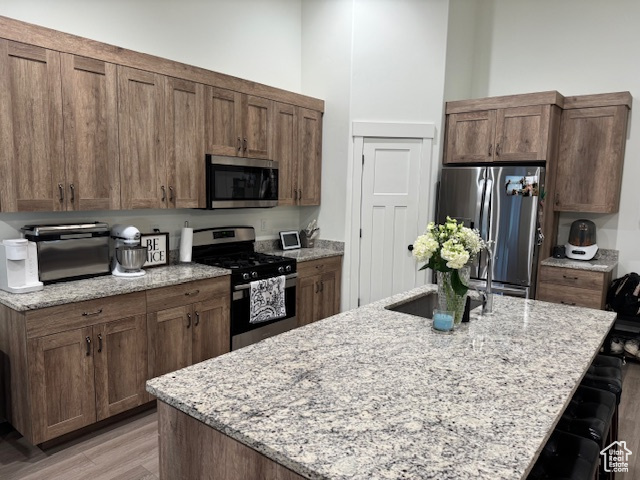 Kitchen featuring light stone counters, a breakfast bar, an island with sink, light wood-style flooring, and stainless steel appliances