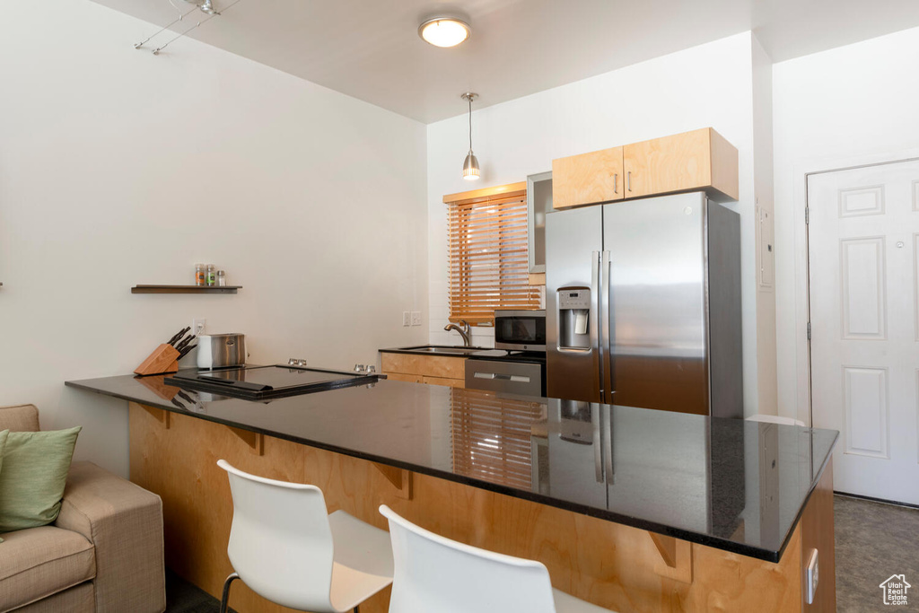 Kitchen featuring a sink, a peninsula, stainless steel appliances, a breakfast bar, and hanging light fixtures