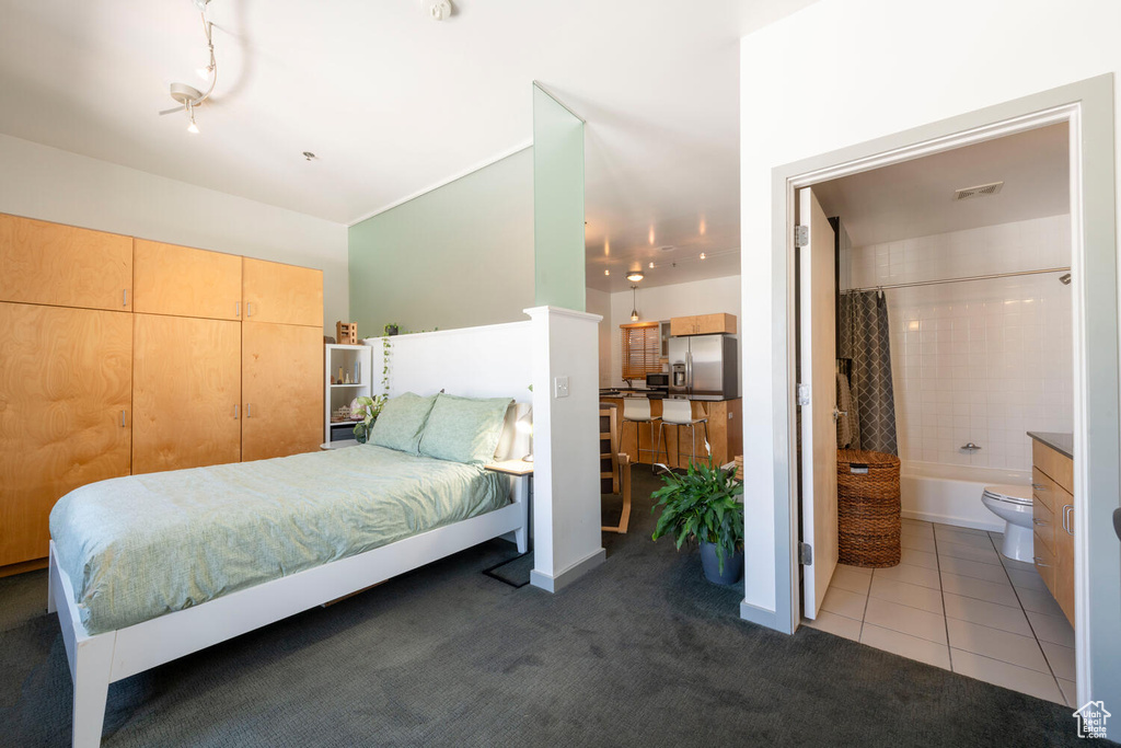 Carpeted bedroom with tile patterned flooring, connected bathroom, stainless steel refrigerator with ice dispenser, and visible vents