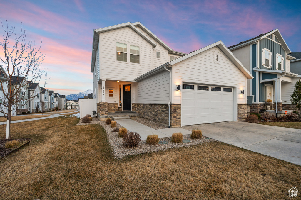 View of front of property featuring stone siding, an attached garage, a residential view, concrete driveway, and a front yard