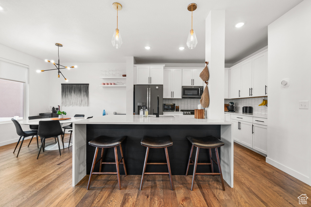 Kitchen featuring appliances with stainless steel finishes, decorative backsplash, wood finished floors, and a breakfast bar