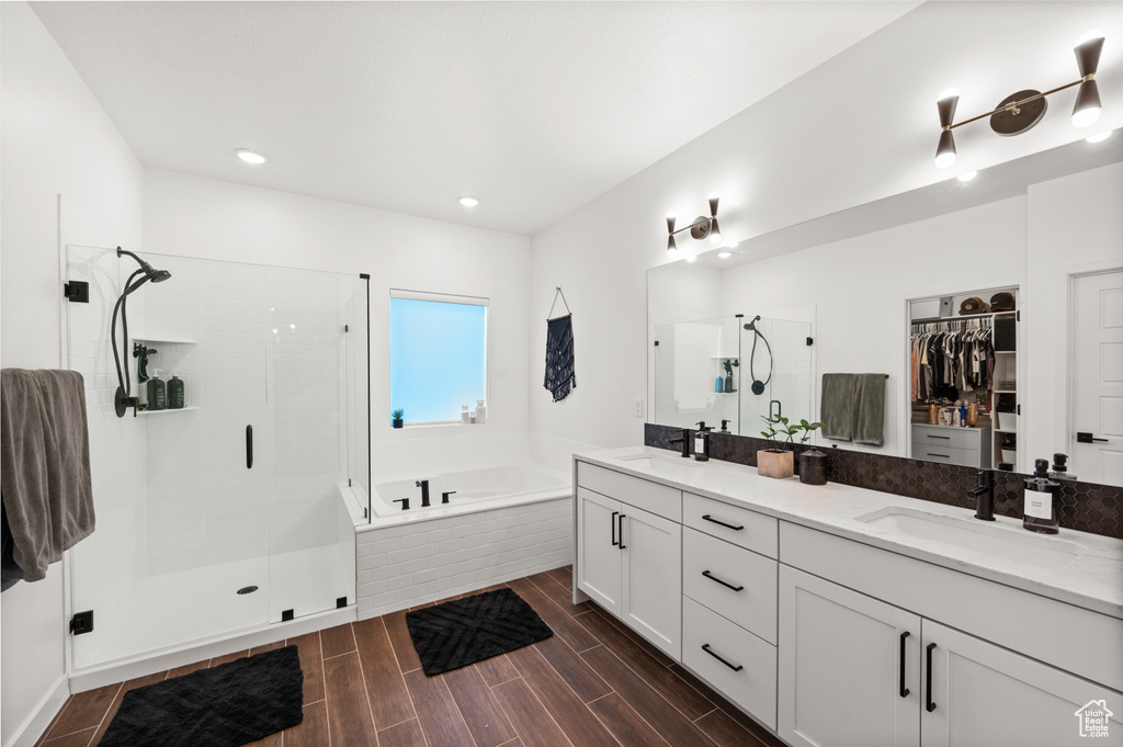 Bathroom featuring a sink, a stall shower, a spacious closet, double vanity, and a garden tub
