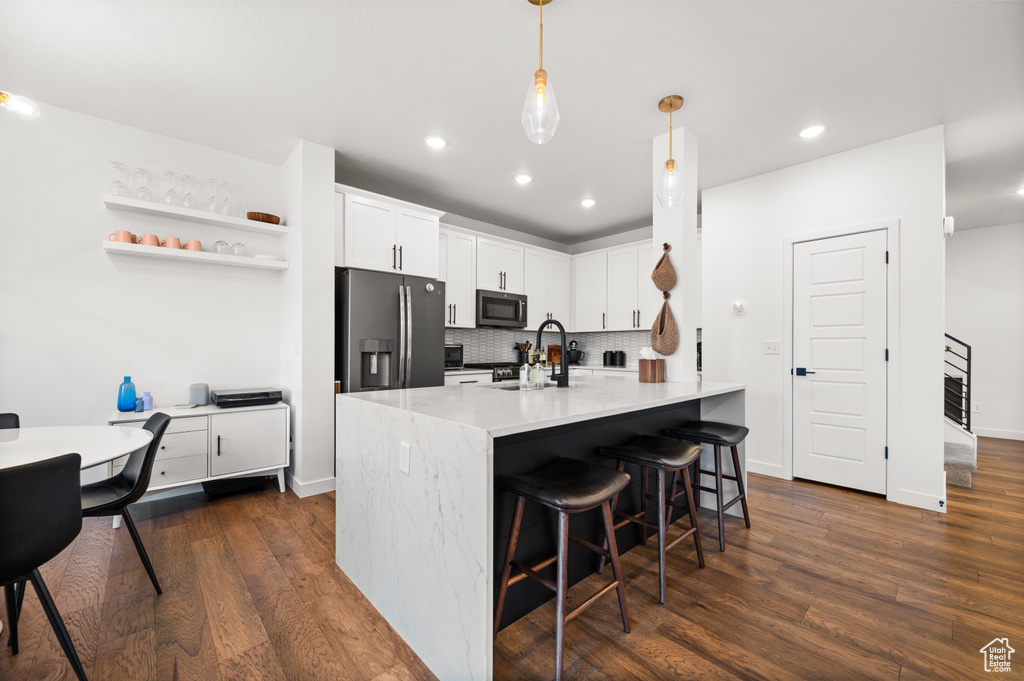 Kitchen with stainless steel appliances, a kitchen breakfast bar, dark wood-style floors, tasteful backsplash, and recessed lighting