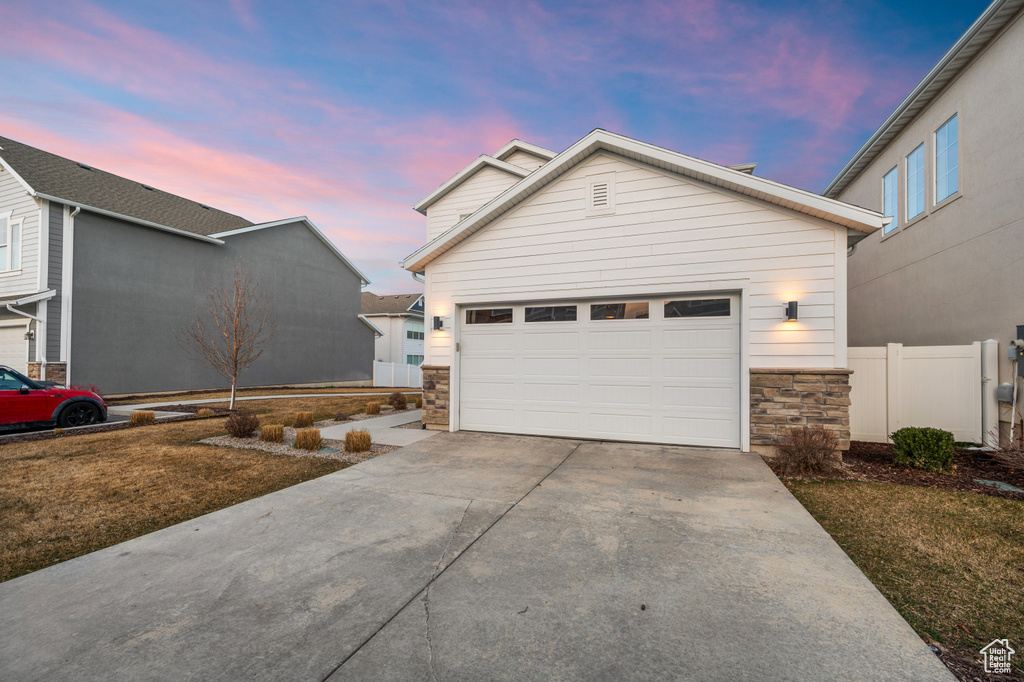 View of front of house with stone siding, concrete driveway, and fence