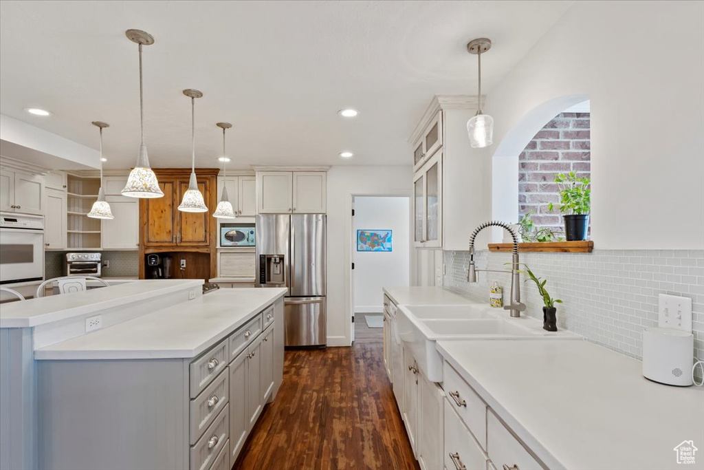 Kitchen with a kitchen island, backsplash, light countertops, and stainless steel refrigerator with ice dispenser