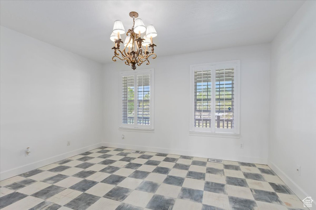 Unfurnished room featuring a chandelier and baseboards