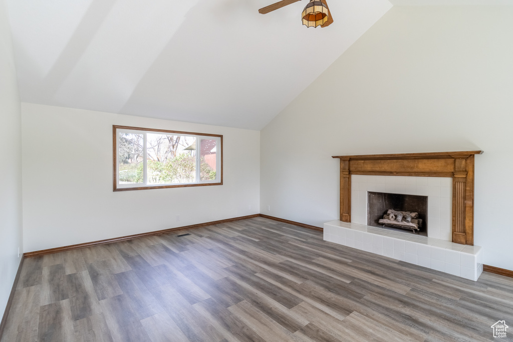 Unfurnished living room with a ceiling fan, a tile fireplace, wood finished floors, and vaulted ceiling