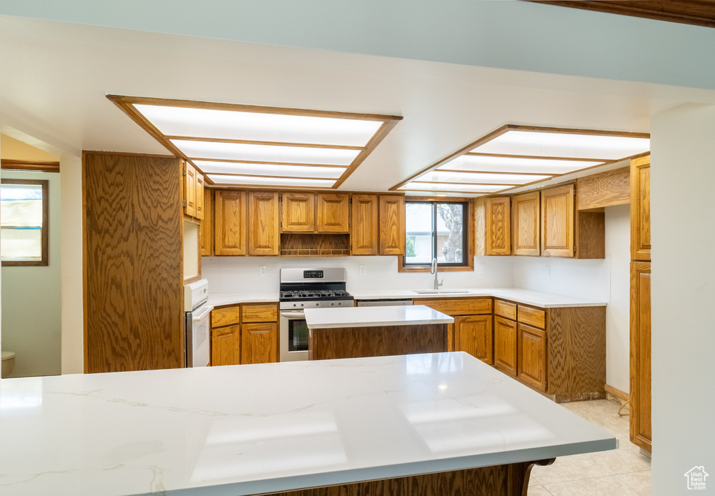 Kitchen with stainless steel range with gas cooktop, brown cabinetry, a kitchen island, light countertops, and a sink
