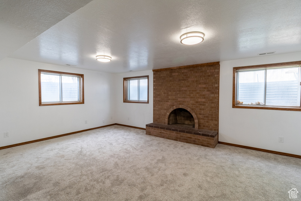 Unfurnished living room featuring baseboards, carpet, a brick fireplace, and a textured ceiling