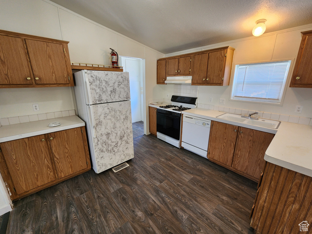 Kitchen with white appliances, a sink, vaulted ceiling, under cabinet range hood, and dark wood finished floors