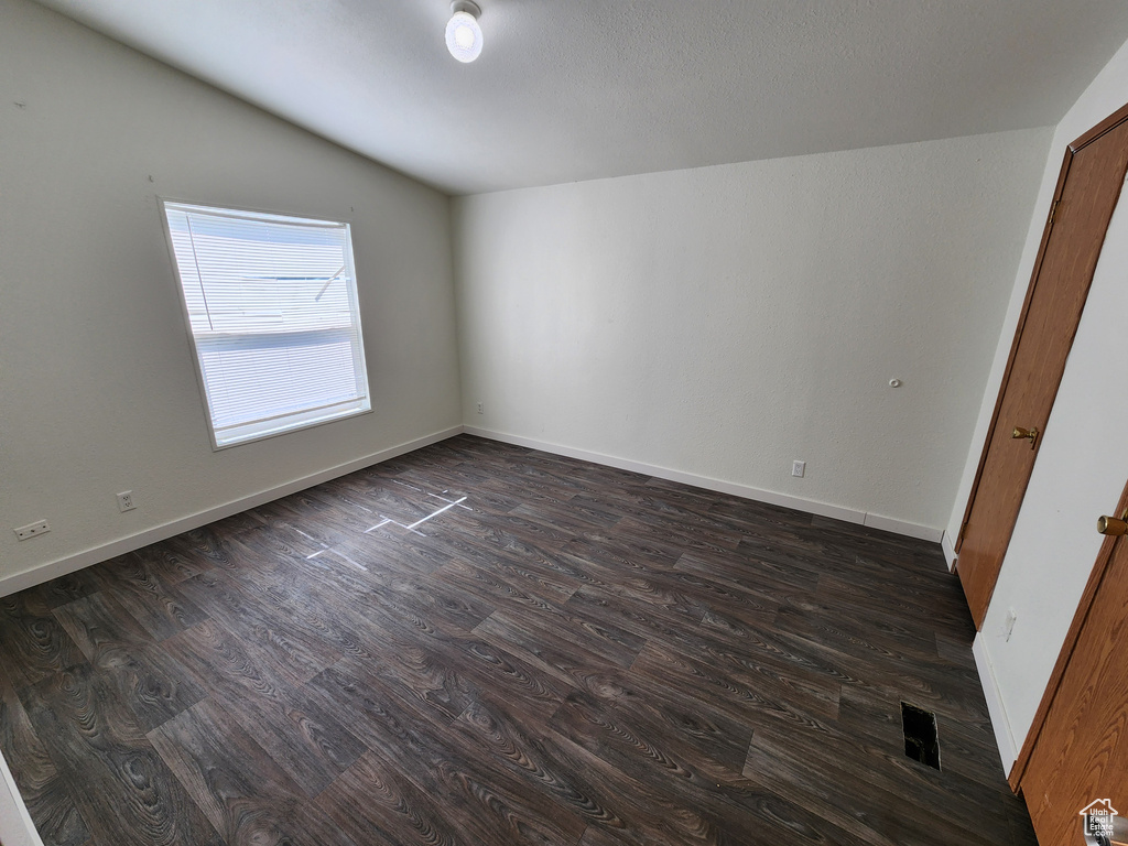 Empty room with dark wood-style floors, vaulted ceiling, and baseboards