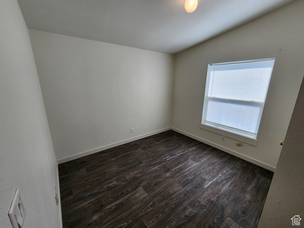 Unfurnished room featuring dark wood-type flooring, baseboards, and vaulted ceiling