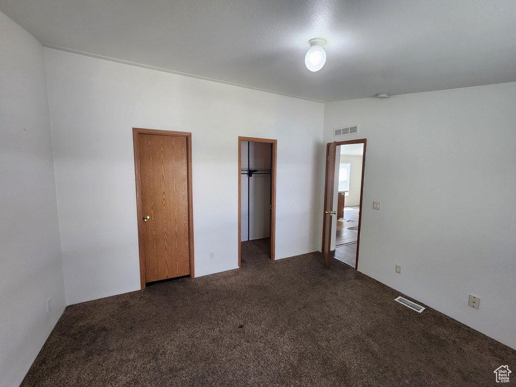 Unfurnished bedroom with carpet flooring, visible vents, and two closets