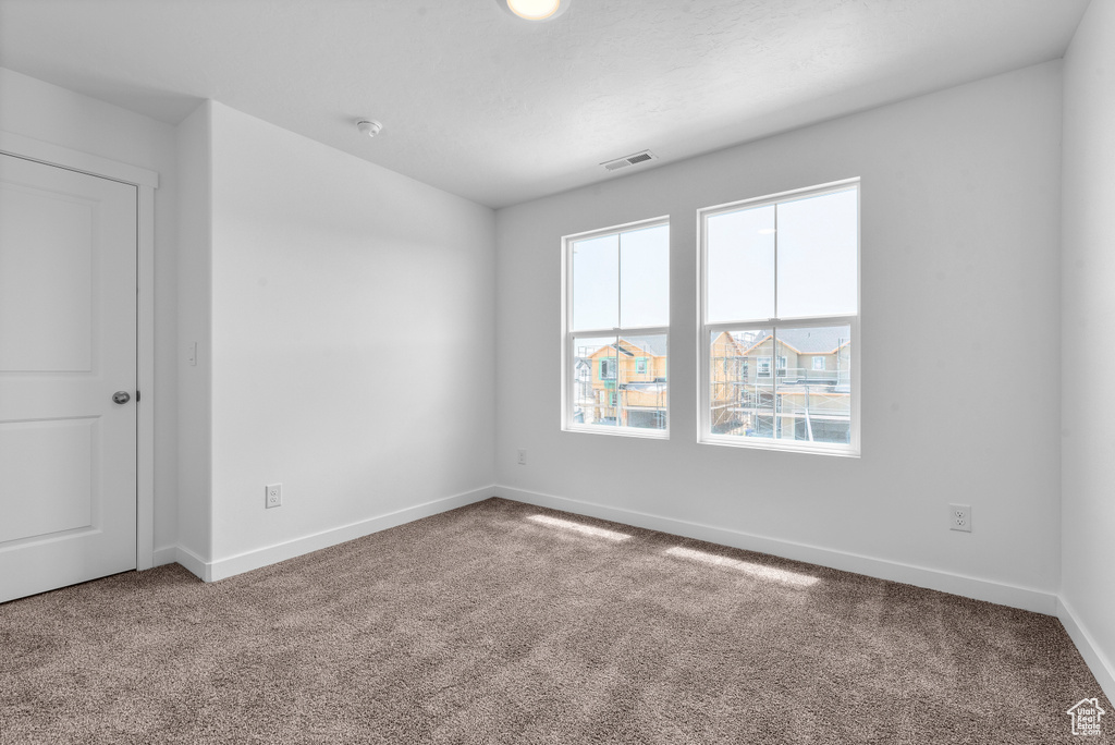 Empty room with carpet, visible vents, and baseboards