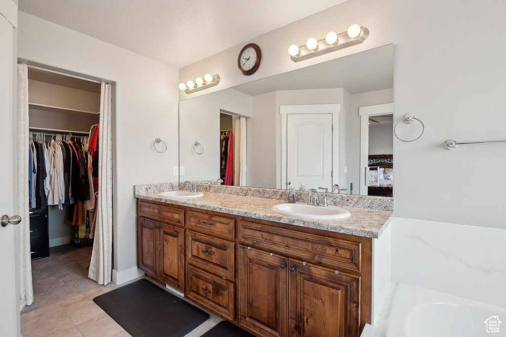 Bathroom with a tub, double vanity, a walk in closet, and a sink