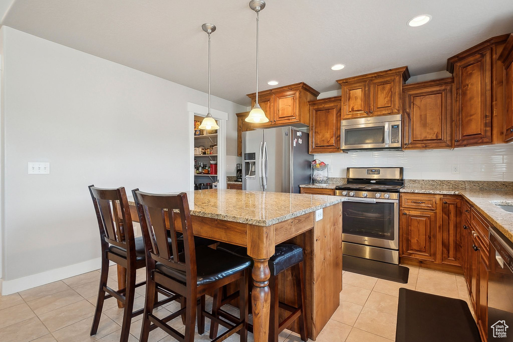 Kitchen featuring light tile patterned floors, a kitchen breakfast bar, appliances with stainless steel finishes, a kitchen island, and light stone counters