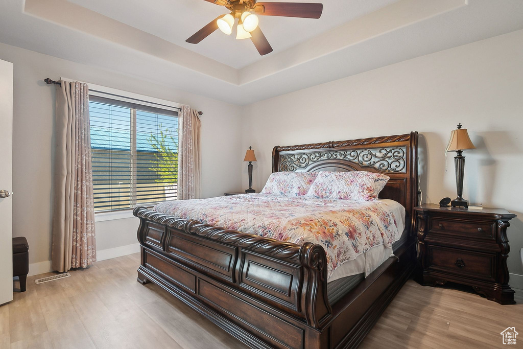 Bedroom with baseboards, a raised ceiling, visible vents, and wood finished floors