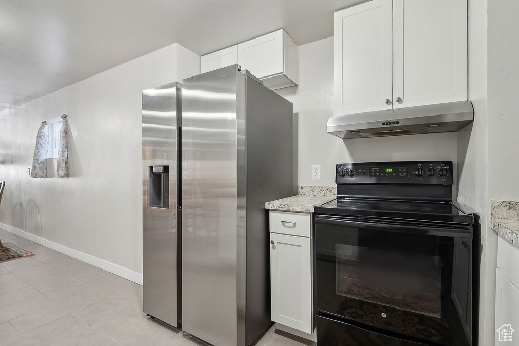 Kitchen with stainless steel refrigerator with ice dispenser, under cabinet range hood, black range with electric stovetop, white cabinets, and baseboards