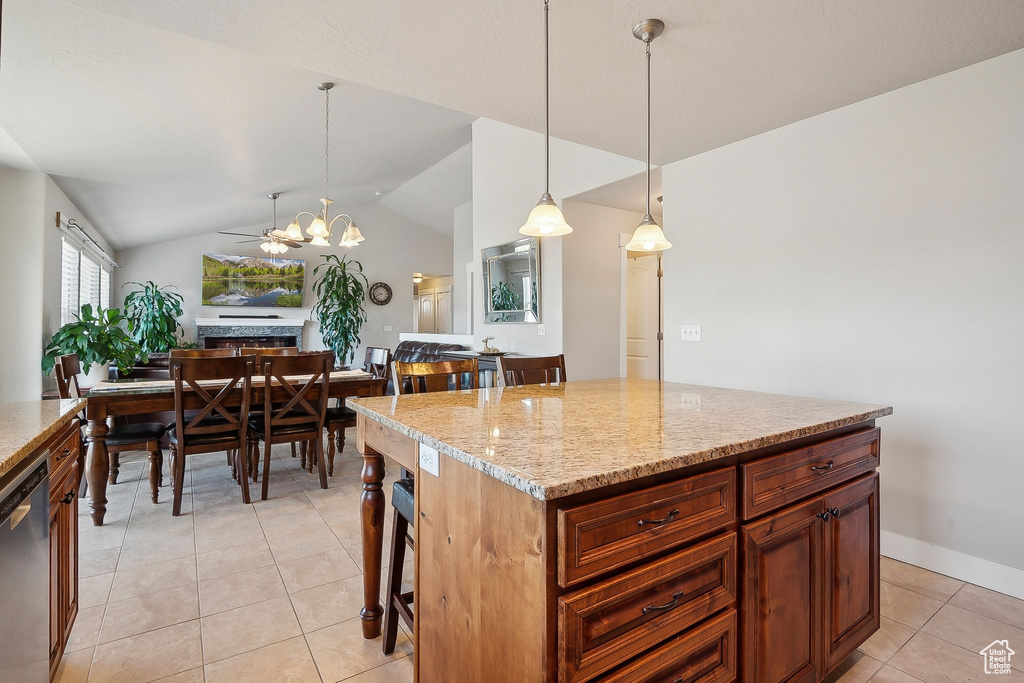 Kitchen with decorative light fixtures, light stone counters, vaulted ceiling, light tile patterned floors, and stainless steel dishwasher
