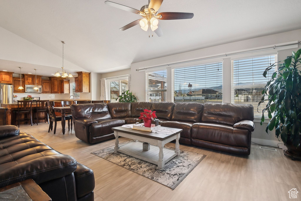 Living room with visible vents, light wood-style flooring, lofted ceiling, and ceiling fan with notable chandelier