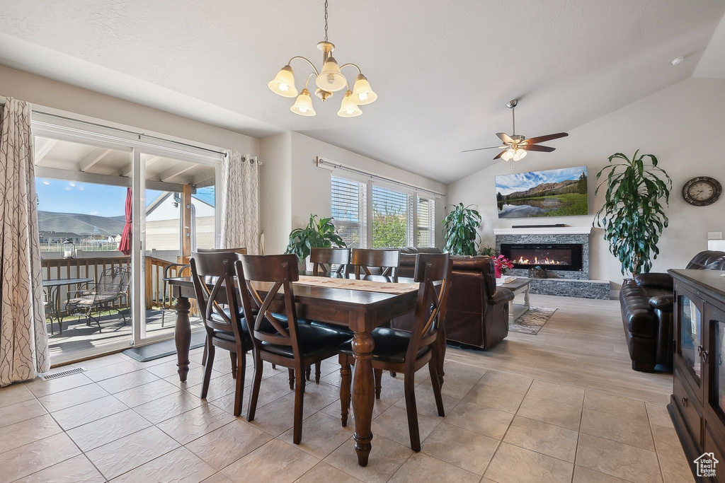 Dining room with lofted ceiling, a fireplace, light tile patterned flooring, and ceiling fan with notable chandelier