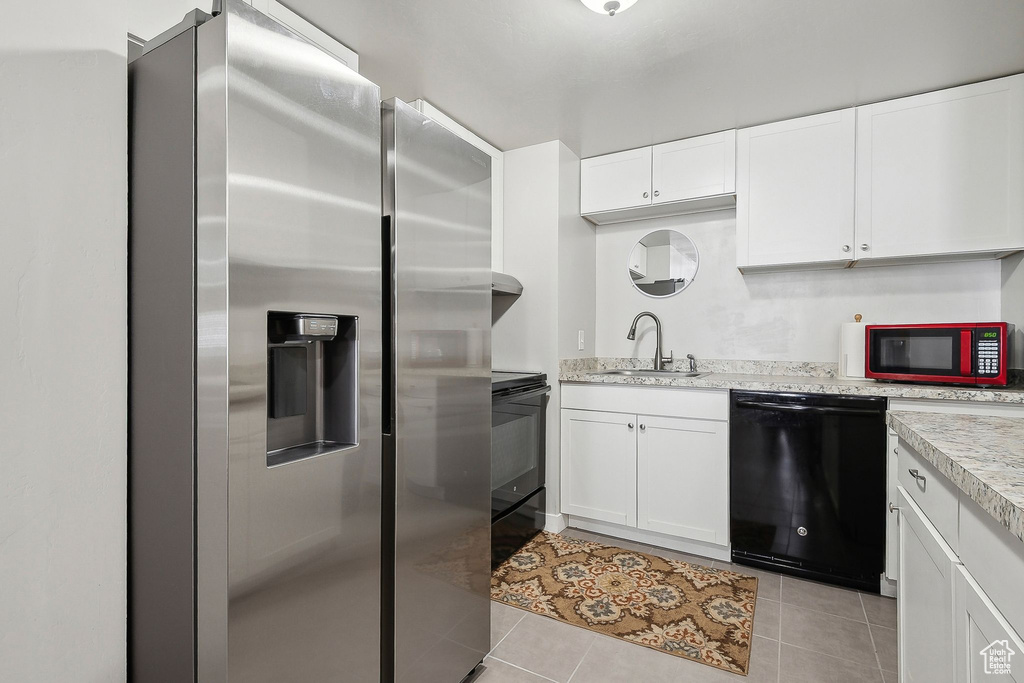 Kitchen featuring white cabinetry, black appliances, light tile patterned floors, and a sink
