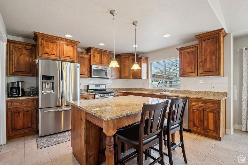 Kitchen with backsplash, light stone counters, appliances with stainless steel finishes, and a sink