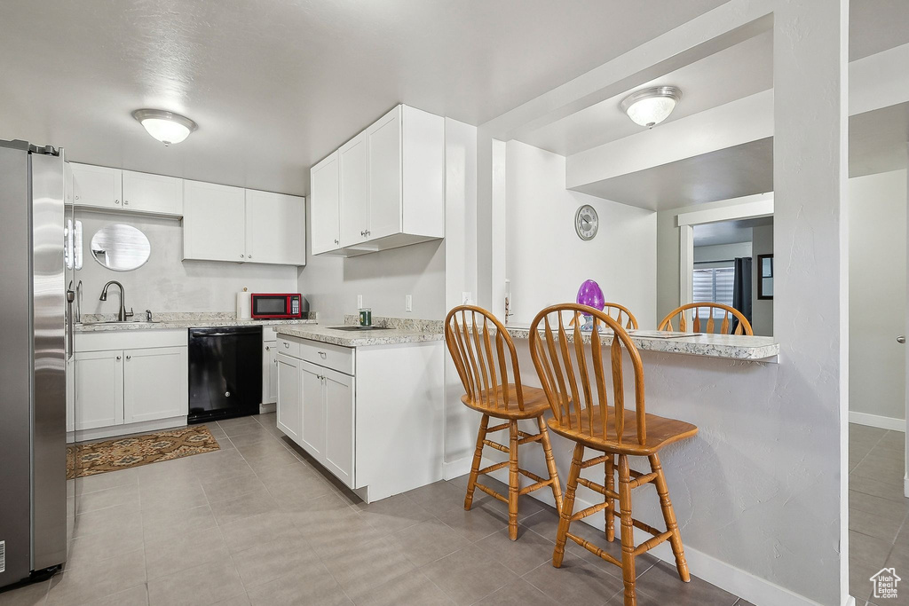 Kitchen featuring freestanding refrigerator, white cabinetry, black dishwasher, and a sink