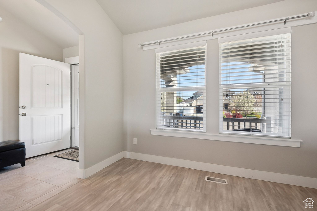 Spare room with light wood-type flooring, visible vents, baseboards, arched walkways, and lofted ceiling