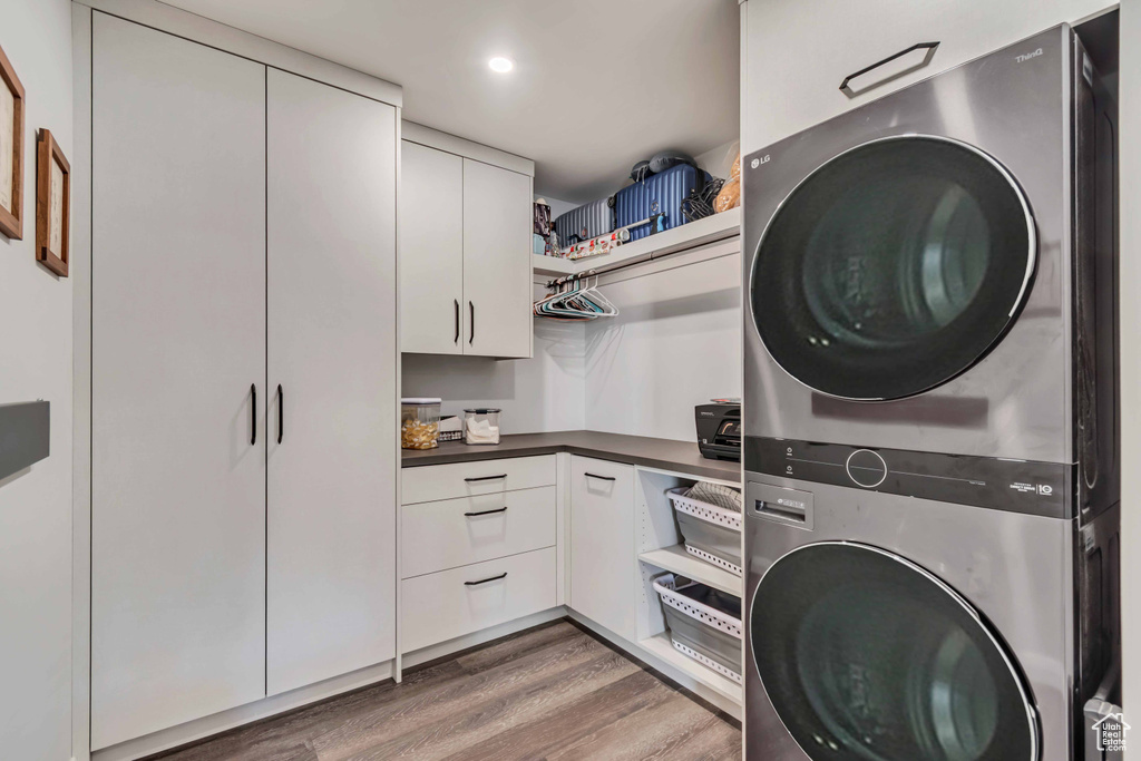 Laundry area with stacked washer / drying machine and wood finished floors