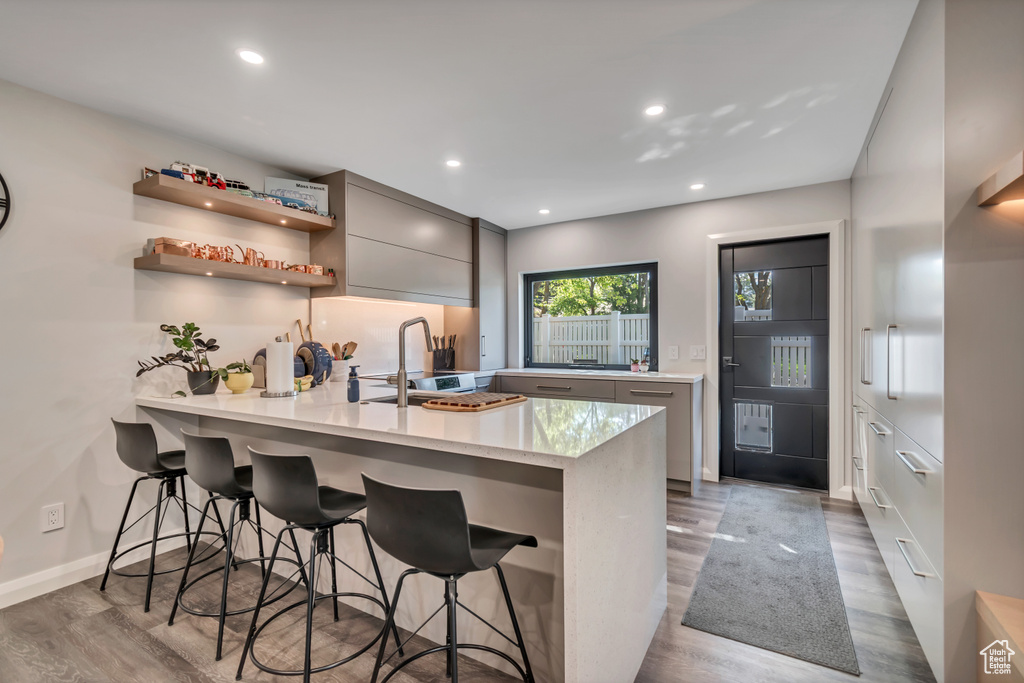 Kitchen featuring a peninsula, gray cabinets, wood finished floors, a breakfast bar area, and modern cabinets