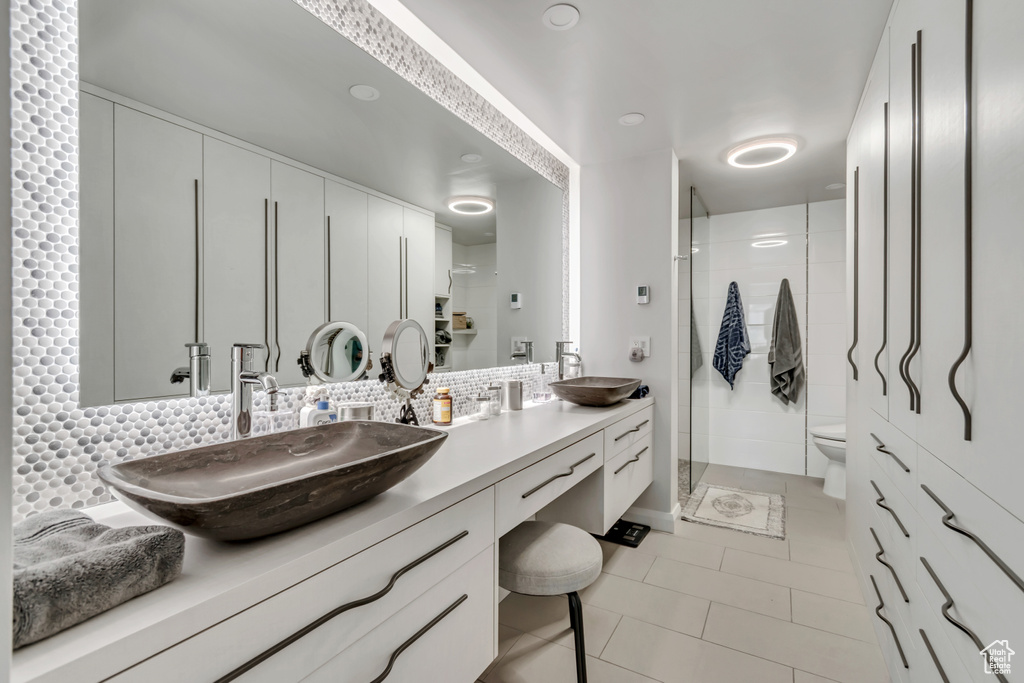 Bathroom with toilet, a sink, tile patterned flooring, a shower stall, and tasteful backsplash
