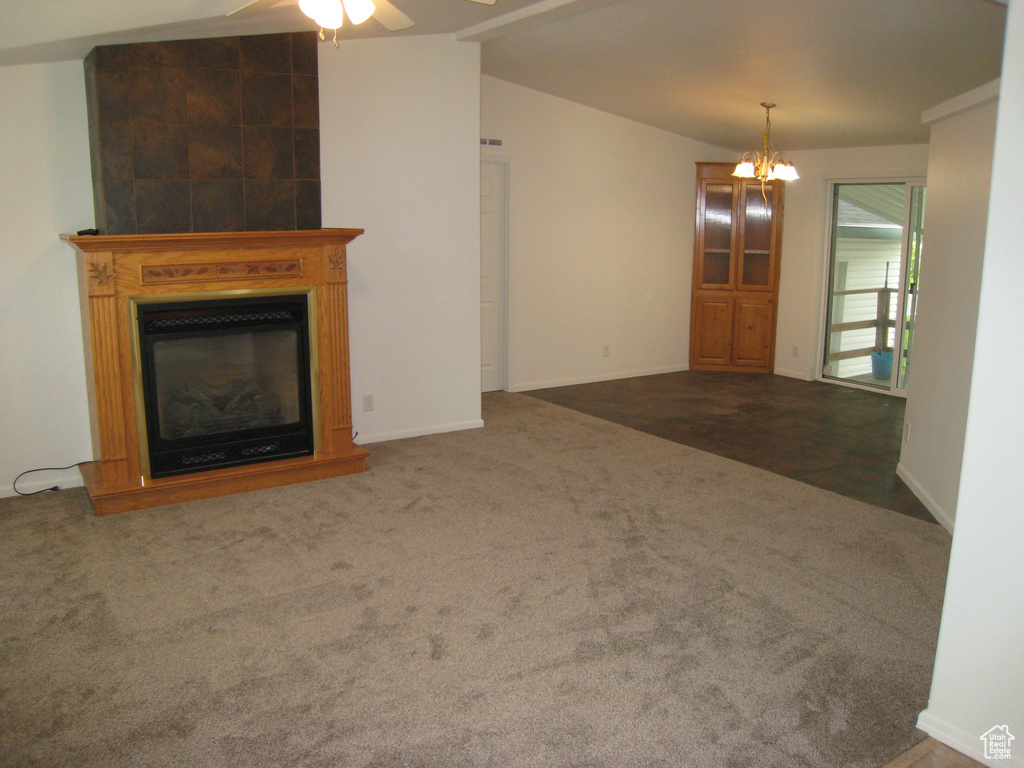 Unfurnished living room with ceiling fan with notable chandelier, a fireplace, carpet floors, baseboards, and lofted ceiling