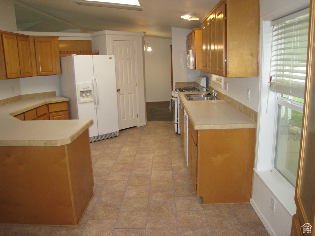 Kitchen with a peninsula, a sink, brown cabinetry, white appliances, and light countertops
