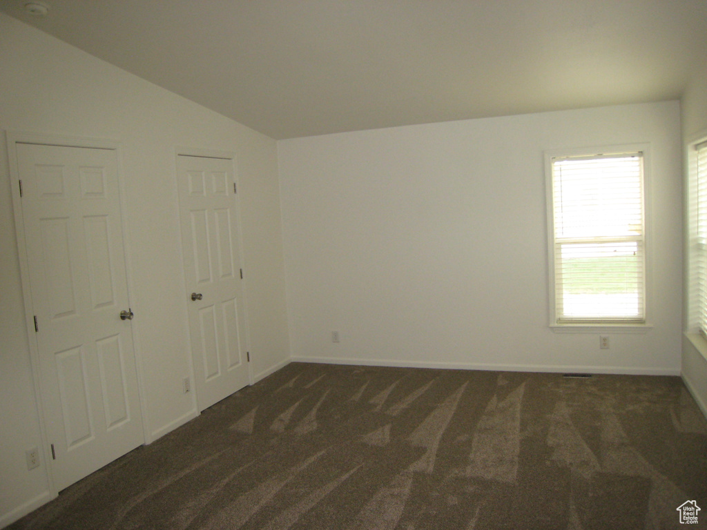 Carpeted empty room featuring vaulted ceiling and baseboards