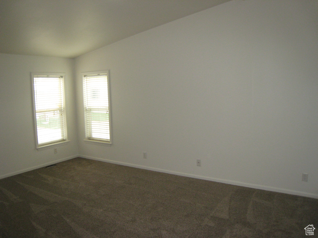 Unfurnished room with visible vents, baseboards, lofted ceiling, and dark carpet