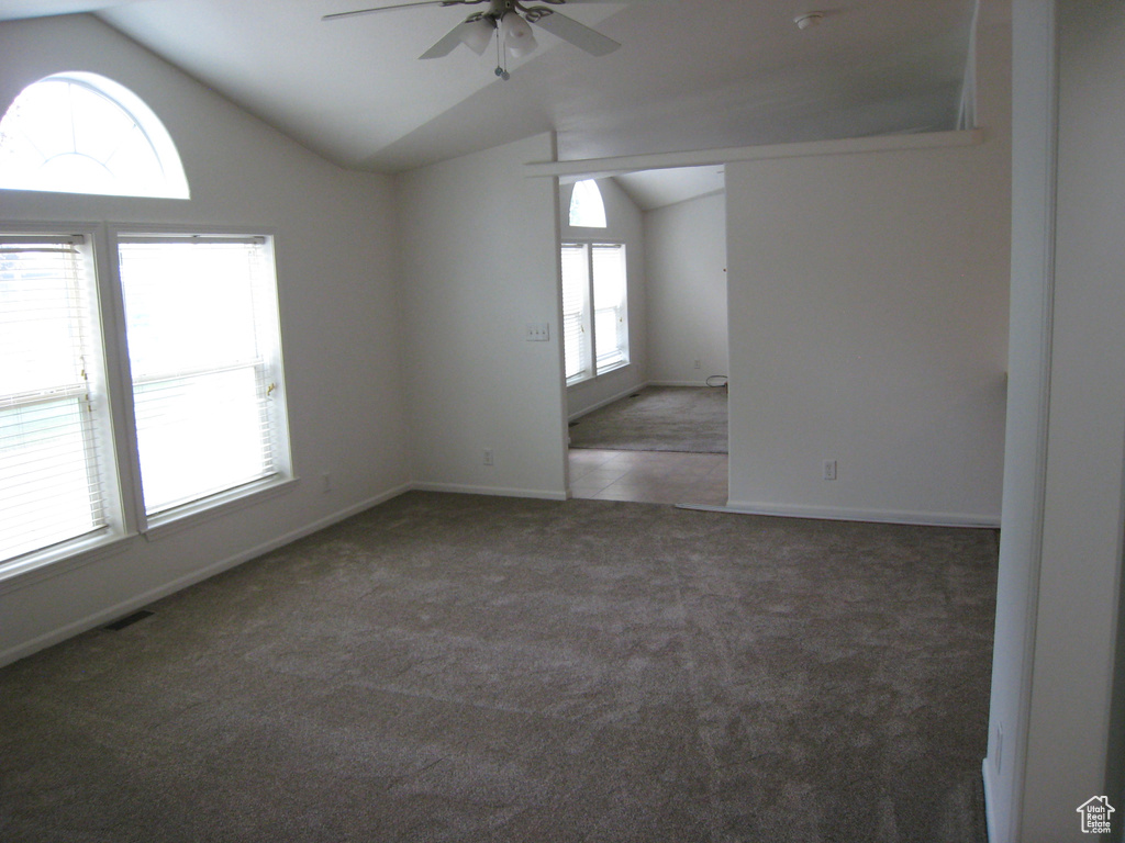 Carpeted spare room featuring vaulted ceiling, baseboards, a ceiling fan, and visible vents
