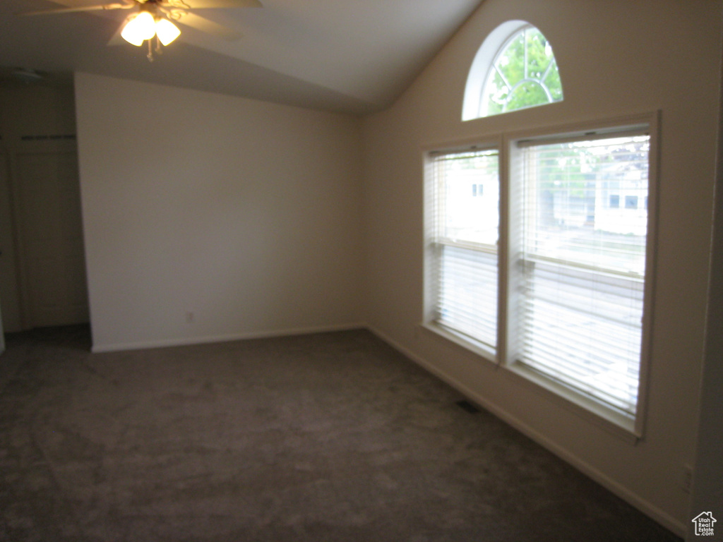 Empty room featuring vaulted ceiling, carpet flooring, a ceiling fan, and plenty of natural light