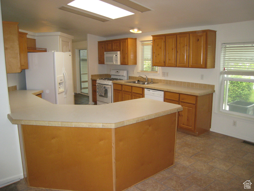 Kitchen with a peninsula, a sink, visible vents, white appliances, and light countertops