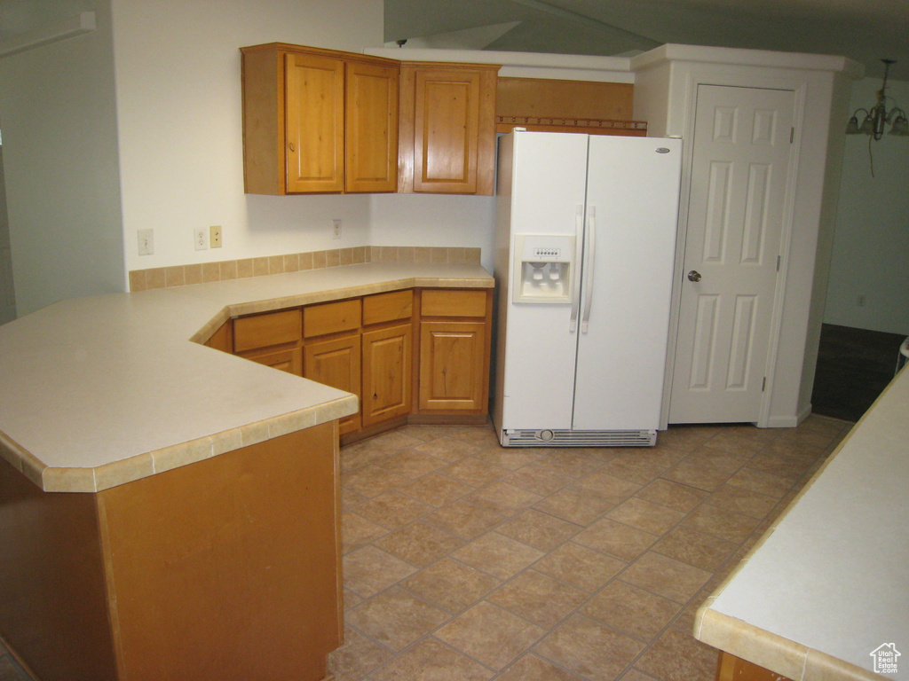 Kitchen featuring a peninsula, brown cabinetry, light countertops, and white fridge with ice dispenser