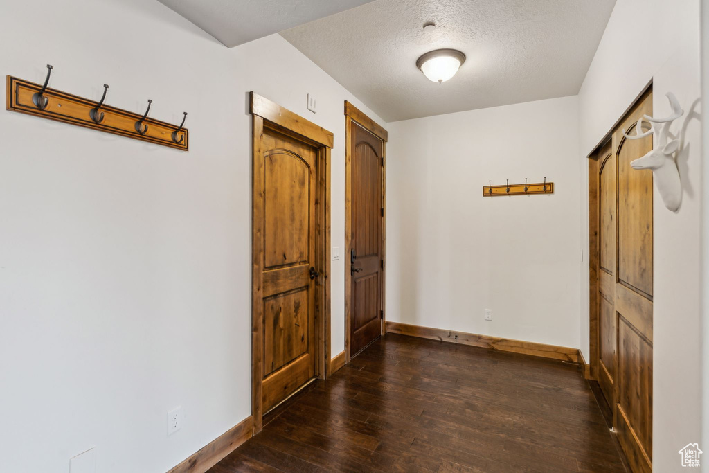 Hall featuring baseboards, dark wood-style floors, and a textured ceiling
